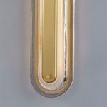 Lit vertical wall sconce showing warm glow illuminating clear glass frame around aged brass center