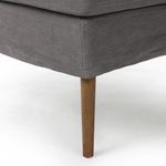 Detail of one amber oak tapered leg beneath relaxed linen skirt extending from seat