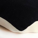 Close-up corner view of pillow showing black textured front and beige back fabric