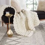 Side view of chunky knit throw draped over dark sofa arm with rug pattern underneath