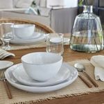 Livia bowl shown on stacked white plates with glassware on wooden dining table in styled room setting