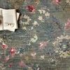 Close-up on rug surface showing texture, floral pattern details, an open book with glasses on top
