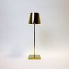 Vera Gold Poldina Pro Table Lamp with sleek gold metal base and cylindrical shade on a square pedestal