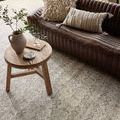 Rug under wooden side table and dark leather sofa with decorative pillows highlighting the rug's pattern variation