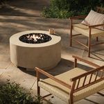 Outdoor patio scene with fire table lit and surrounded by woven and wooden furniture and greenery