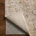 Corner of rug flipped up revealing tightly woven backing and layered rug pad underneath on wood floor