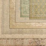 Stacked traditional rugs in various colors and patterns, including tan, green, and mustard hues