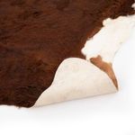 Underside of cowhide rug lifted to reveal smooth, off-white backing with visible stitching