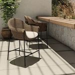 Two woven outdoor stools in patio setting by stone wall and wood countertop, sunlight casting shadows