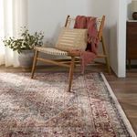Side angle of chair draped with terracotta throw placed partially on Zakaria rug