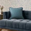 Ocean blue pillow placed on a navy tufted sofa with botanical wallpaper background