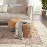 Close-up showing woven poufs and part of the rug’s intricate border near a light textured runner