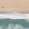 Aerial view of sandy beach with gentle ocean waves and a lone lifeguard tower near the shore