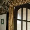 Upper corner of mirror reflecting ribbed glass window pane and framed artworks on floral wallpaper