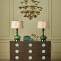 Green lacquer box set styled on wooden dresser with brass accents, flanked by green lamps and gold chandelier overhead