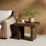 Outdoor setting with table beside rattan chair, natural wall backdrop, and tile flooring
