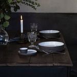 Set of white and gray bowls styled on dark wooden table with glassware, candle, and greenery in atmospheric setting