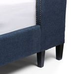 Close-up focus on black tapered leg and fabric corner seam at foot of bed