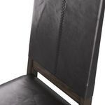 Diagonal close-up of stitched black leather back panel with visible texture and wood frame