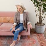 Lifestyle scene with woman sitting barefoot on rug in modern room with pink sofa and plant
