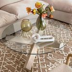 Judy Coffee Table styled in living room setting with beige sofa, patterned rug, and decorative vases on glass surface