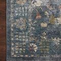 detailed close-up of rug corner showing muted colors, intricate motifs, and fringe on hardwood floor