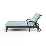 Side view showing curled armrest, aluminum wheels, and reclining back with blue cushions