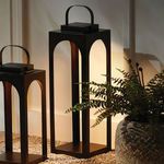 Two bronze lanterns lit at night next to a large planter with greenery on gravel floor