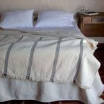 cotton throw spread across bed with black vertical stripes and fringed edges beside wooden nightstand