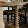 Close-up of spiral-carved leg and parqueted veneer tabletop corner with woven seating chairs in room setting