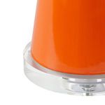 Close-up of the lamp's orange ceramic base showing glossy texture and clear acrylic circular platform