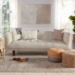 Living room scene with rug under a beige sofa, accented with pillows and textured poufs on wooden floor