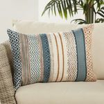 Lumbar pillow styled on outdoor wicker chair with white cushions and green plant background