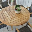 Top-down close-up of round teak dining table surface with decorative planter, surrounded by wicker chairs
