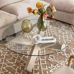 Decorative chain link sculpture on glass coffee table with floral vase and patterned rug backdrop
