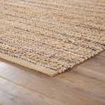 Natural tan and navy solid area rug with mottled gray and navy details, hand-woven rayon and jute texture on wooden floor
