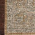 Close-up of rug corner on dark wood showing detailed floral border in muted gold and gray hues