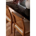 Two Orville chairs tucked under black marble dining table with beige seats and rattan backs