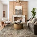 Layla rug in living room setting with brown sofa, white armchair, round brass coffee table, and wood accent wall