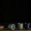 Five ceramic cups in different earth-tone colors displayed in a row on rustic wooden surface against black background