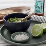 Seed grey bowl with guacamole and cilantro, placed on green plate with lime halves and salt