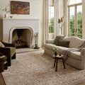 rug styled in a living room with sofa, green chair, fireplace, and tall windows showing overall room context