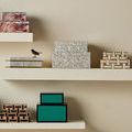 Multiple decorative boxes including Aarna set displayed on two white shelves against beige wall
