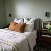 Bedroom interior with two Kira 2 Light Wall Sconces mounted on light green walls above wood nightstands on either side of ...