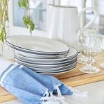 Side view of stacked white Beja plates with blue rim, accompanied by blue-striped napkins and glassware on wooden board