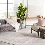 Living room styled with rug beneath velvet purple sofa and plants by large black-framed window