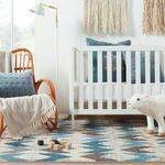 Nursery scene with chevron rug, white crib, rocking chair with blue cushion, and hanging macrame