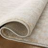 Close-up of Kamala rug rolled to reveal dense pile and woven backing on wood floor