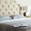 Close-up of tufted fabric headboard with portion of bedspread, pillows, and lamp in soft lighting