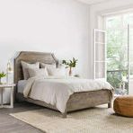Beige linen and cashmere duvet on a wooden bed in a bright room with neutral decor and natural light